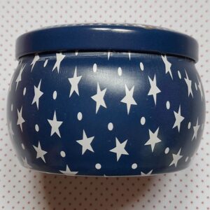 Vue de côté d'une boite ronde vintage contenant une bougie parfumée, la couleur est bleue nuit et elle est décorée d'étoiles et de points blanc